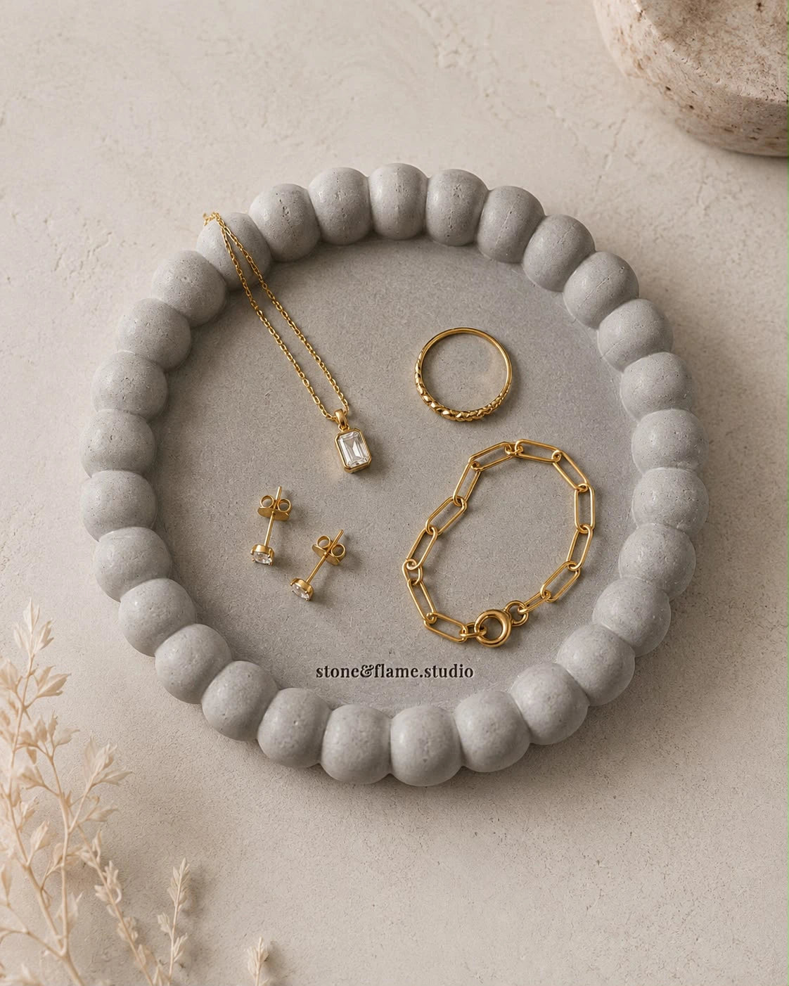 צלחת תכשיטים בטון אפור flatlay — שרשרת, צמיד ועגילים על רקע אבן